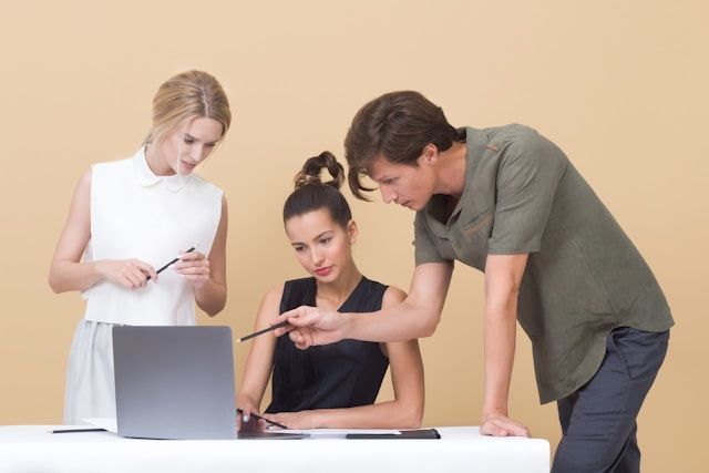 Mann unterrichtet Frau und zeigt auf grauen Laptop